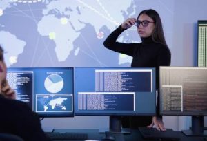 Smiling cyber security team working in a Cyber Security Operations Center (SOC). Woman work as Chief Information Security Officer (CISO) and manager pointing on a real time map om tablet.